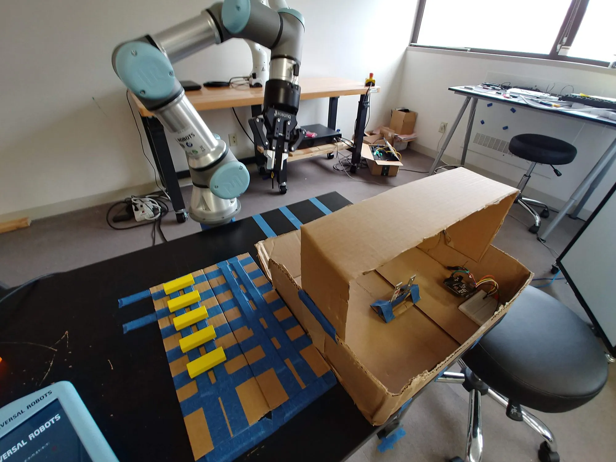 The whole bench: the UR3e, the box, the taped grid of blocks, and the pendant at the near corner.