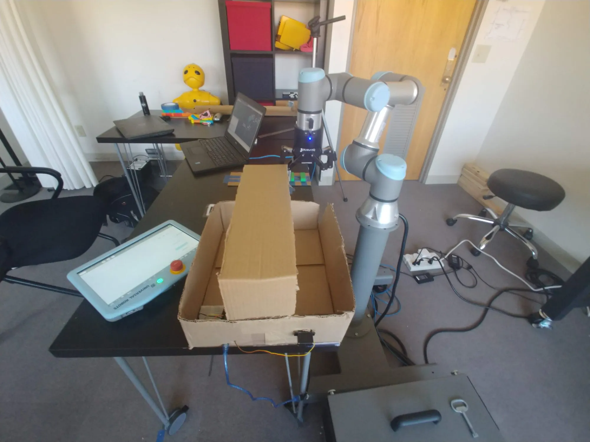The UR3e reaching into a cardboard box on the table, August 2019.