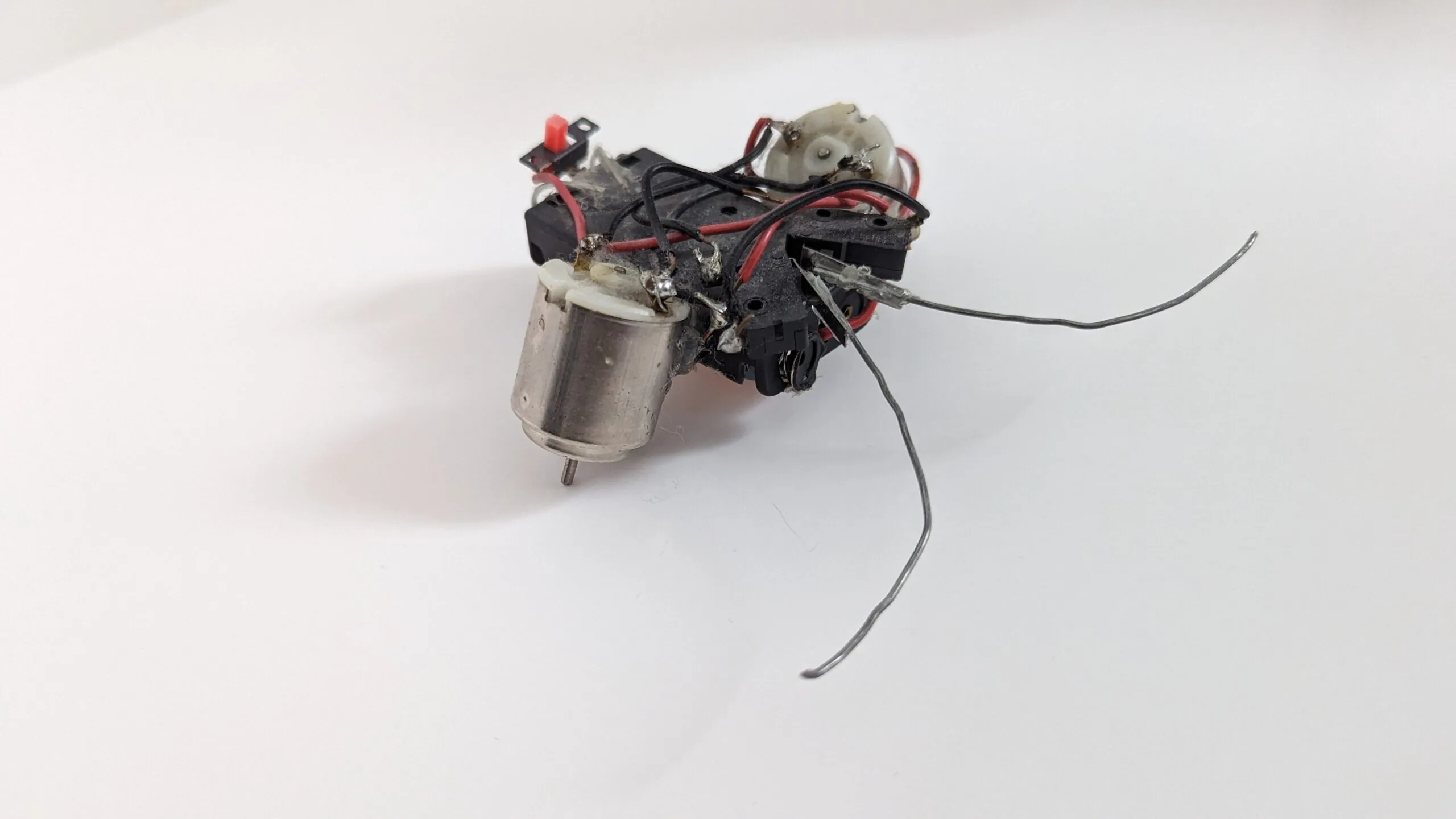 Three-quarter view of a Beetle: two toy motors on a battery-holder chassis, red power switch on top, bent wire feelers.