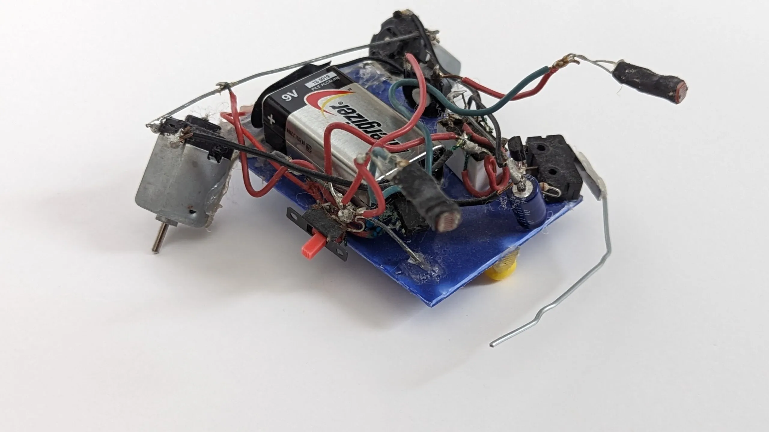 Herbie today: 9V strapped over the blue chassis, drive motor on the left, photoresistors and whisker reaching forward.