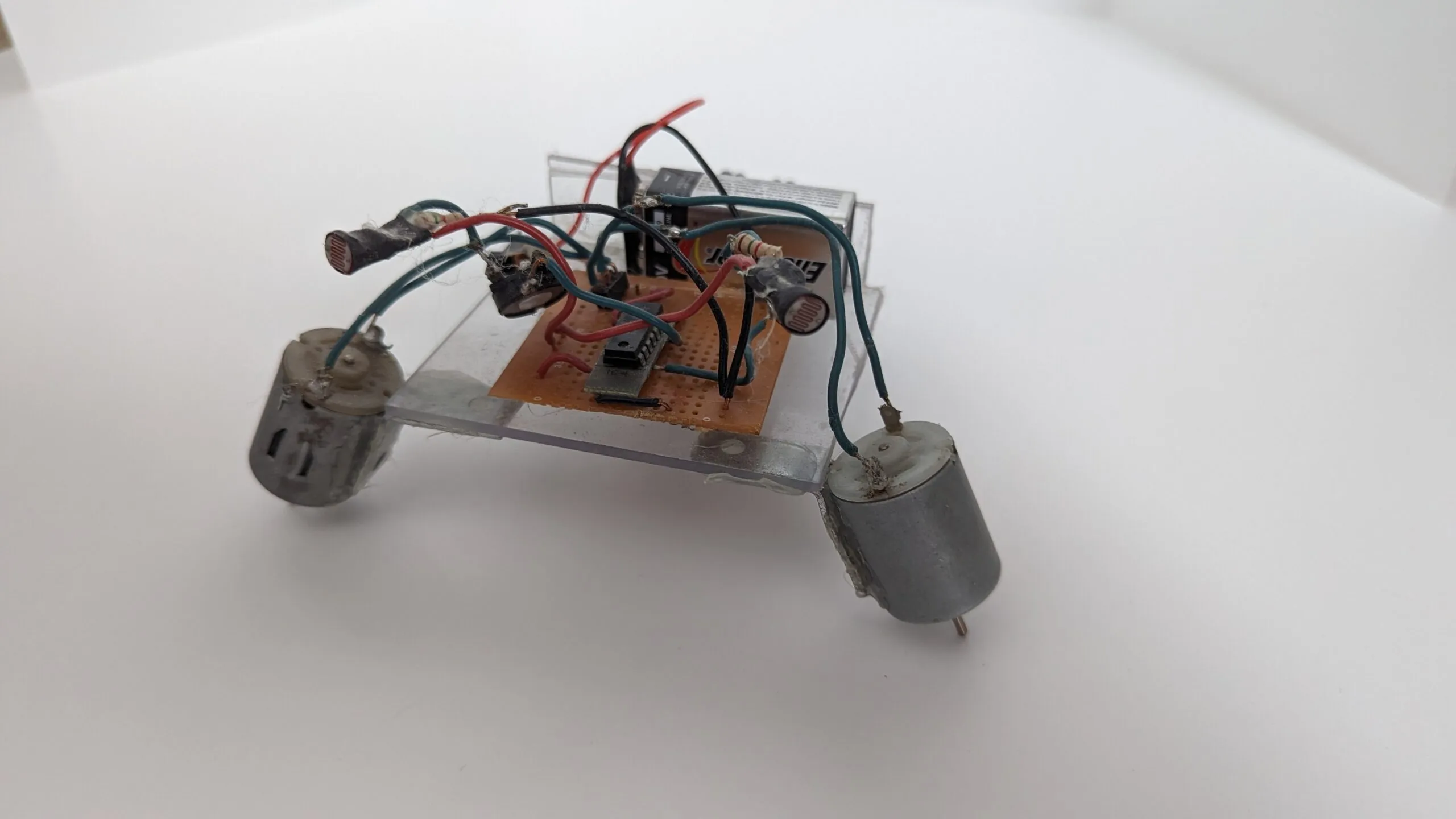 NoBB from the side: photoresistors arcing over the protoboard on long leads, motors angled down as legs.