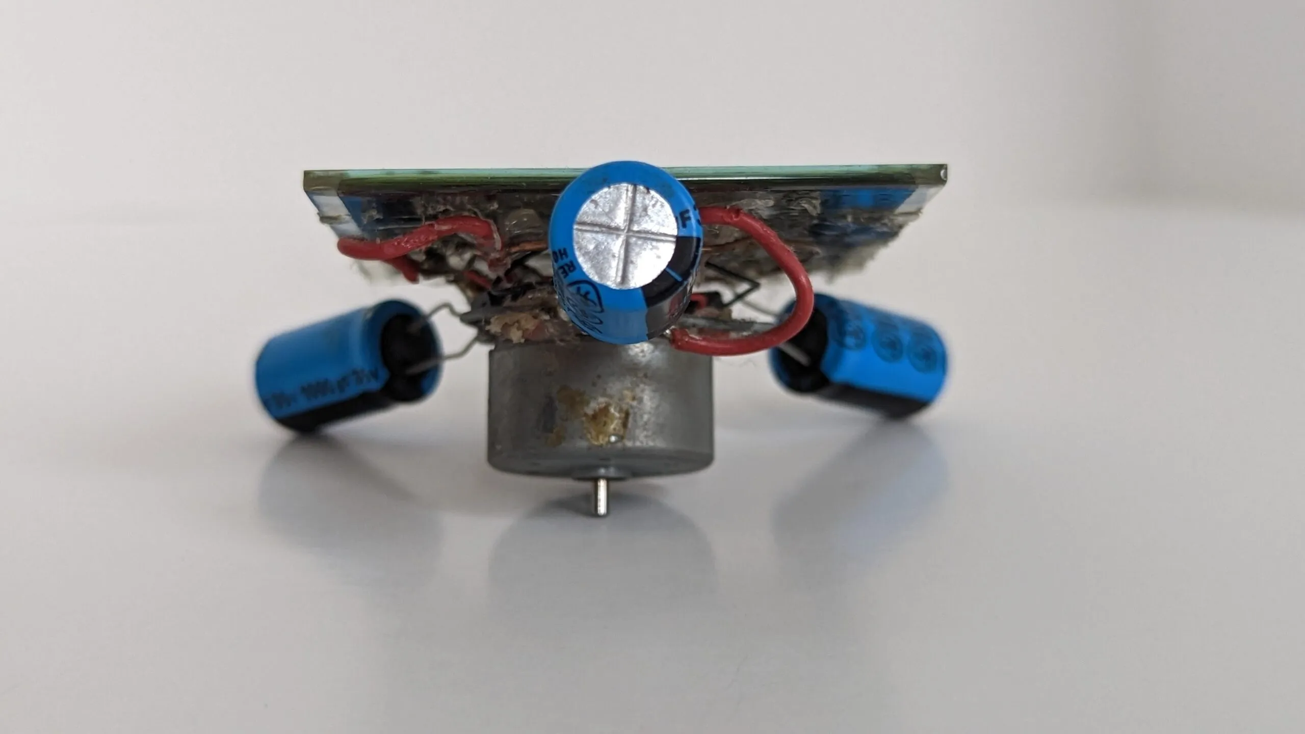 Head-on view of the Symet at table level, motor in the middle and capacitor feet splayed to both sides.