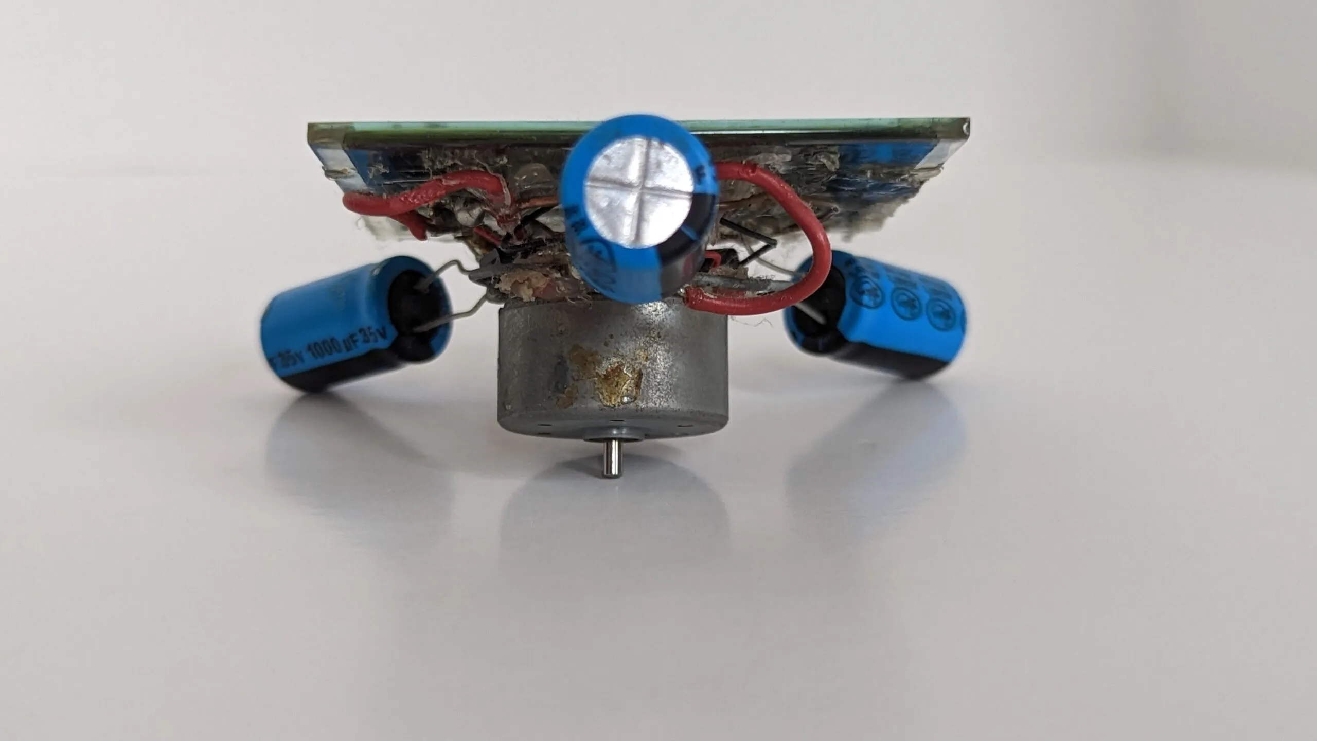 Underside of the Symet: the salvaged CD player motor hangs below the solar cell with the three capacitor feet angled out.