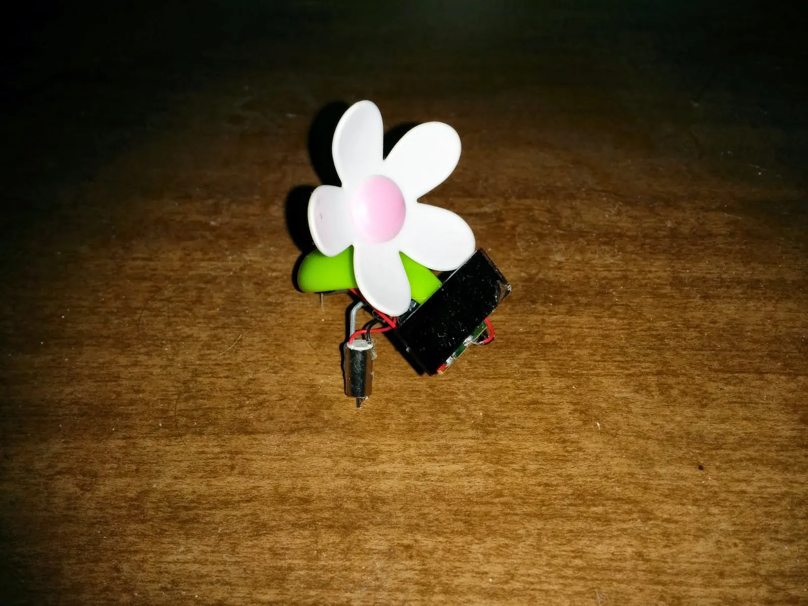 SymFlower v1: a plastic daisy on a green stem over a small solar panel, pager-motor foot below.