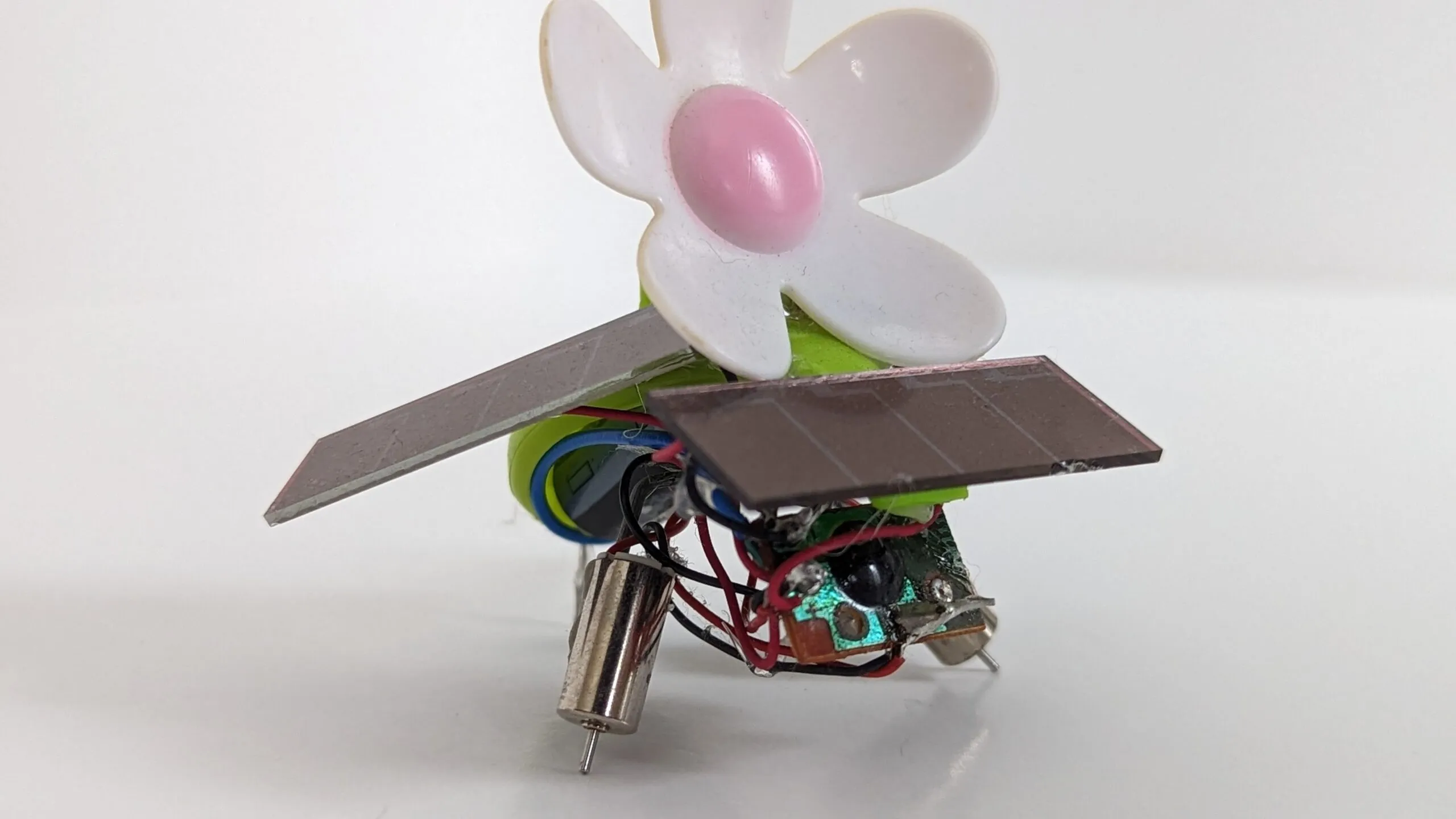 Close side view of SymFlower v2: mirrored solar wings spread under the daisy, twin pager motors as legs.