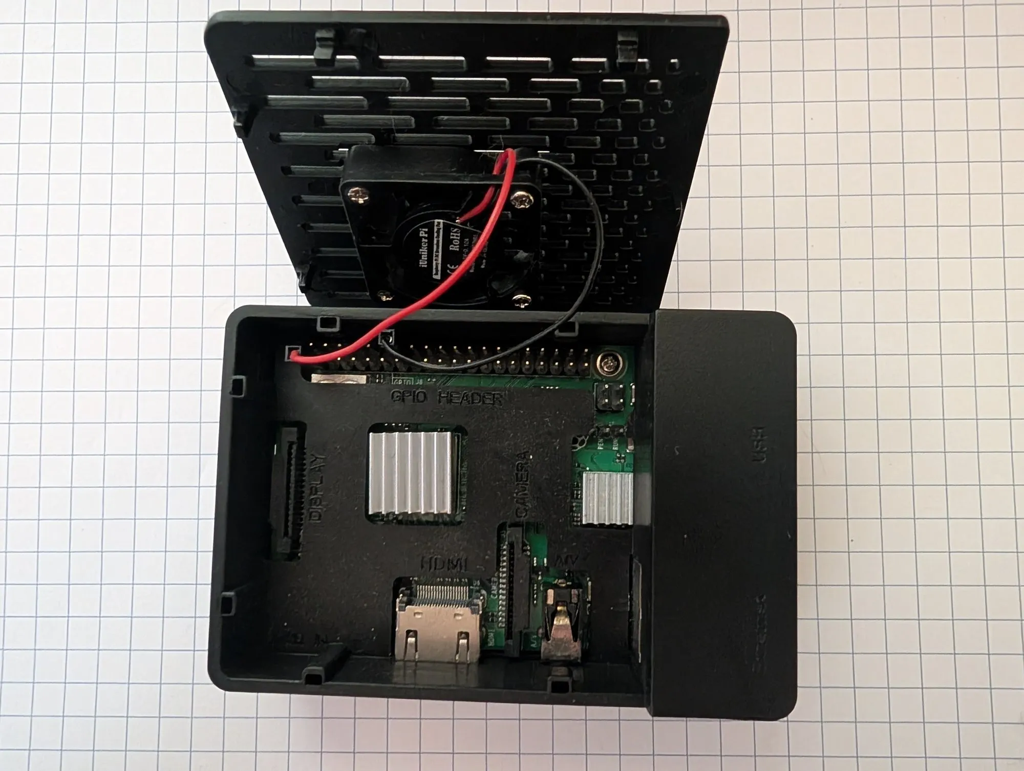 The Raspberry Pi 3B+ in its black case with the lid flipped open, a small fan mounted in the lid wired to the board, and heatsinks on the chips.