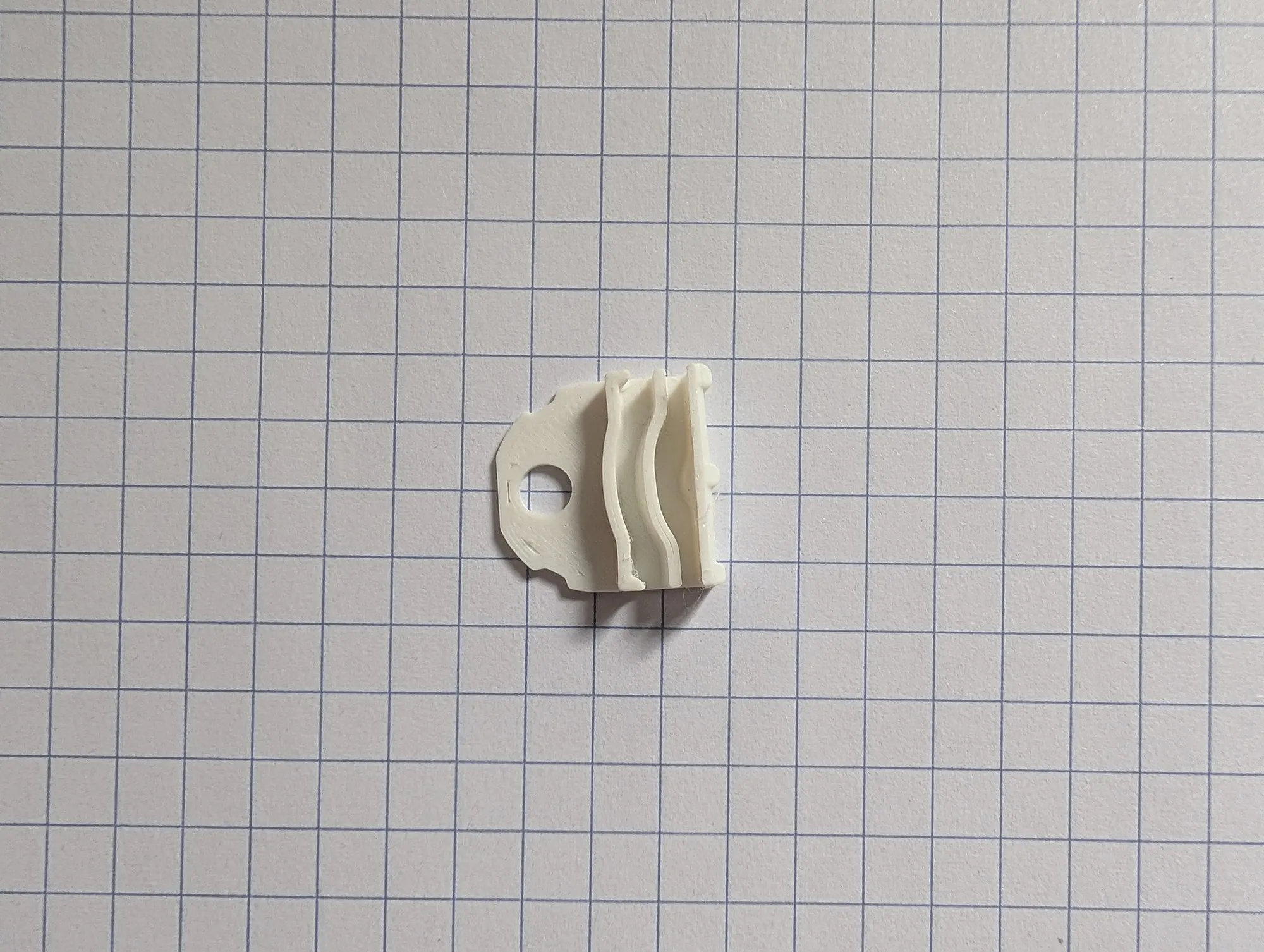A small white 3D printed filament clip lying on grid paper.