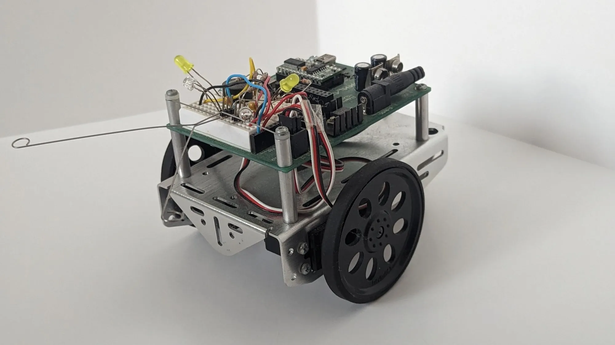 Three-quarter view of the BOE-Bot from the left, aluminum chassis and black wheel in front, whisker out.