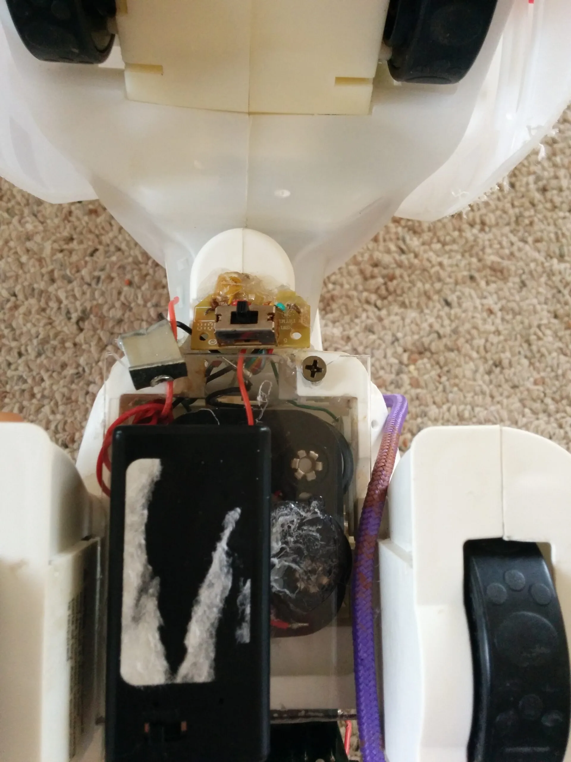 Bubbles' underside: four C batteries and a 9V battery, the relocated power switch hot glued in place, and a paw at the edge of frame.