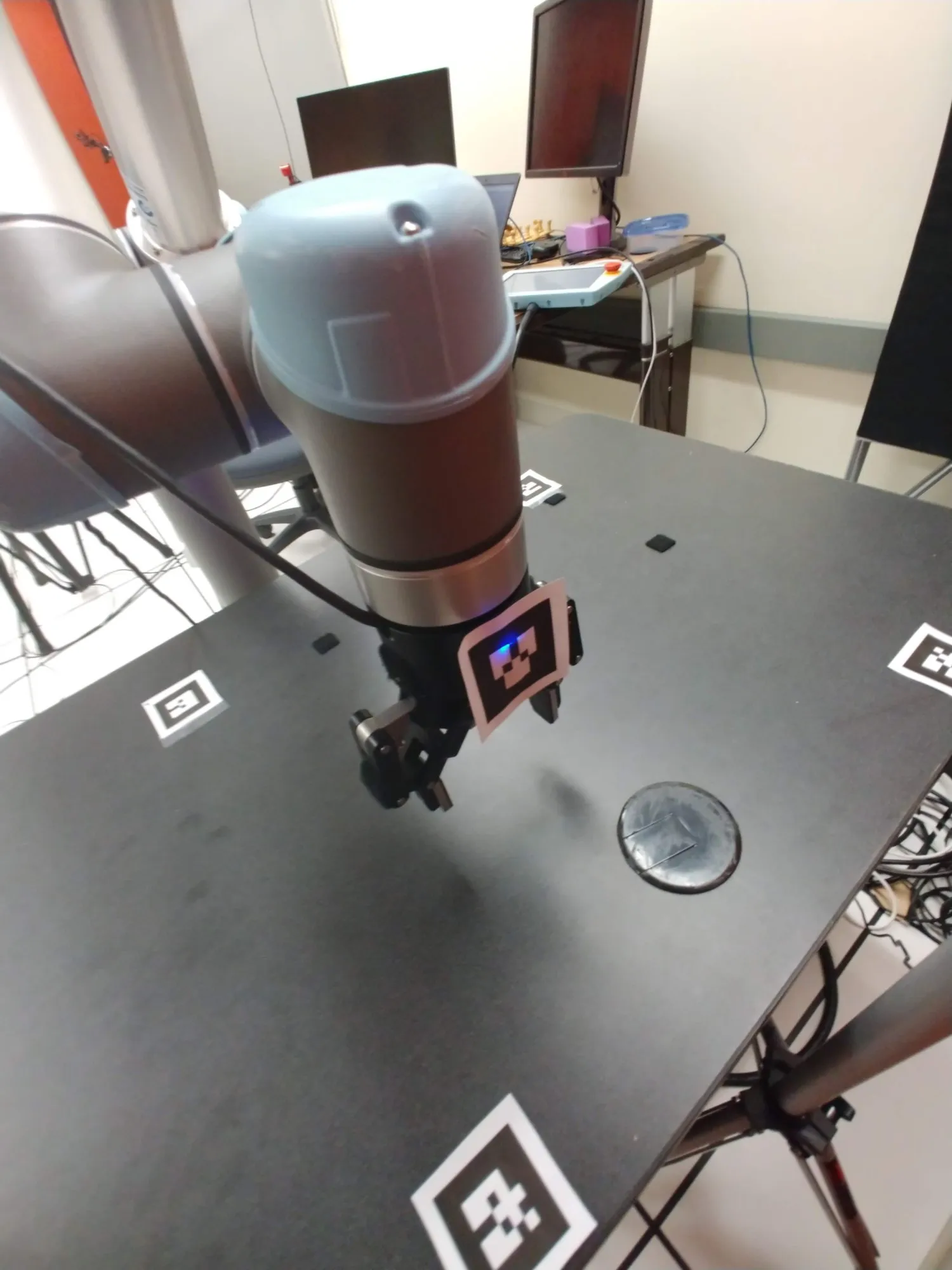 The gripper hovering over the black table, an ArUco tag under it and another at the table corner.