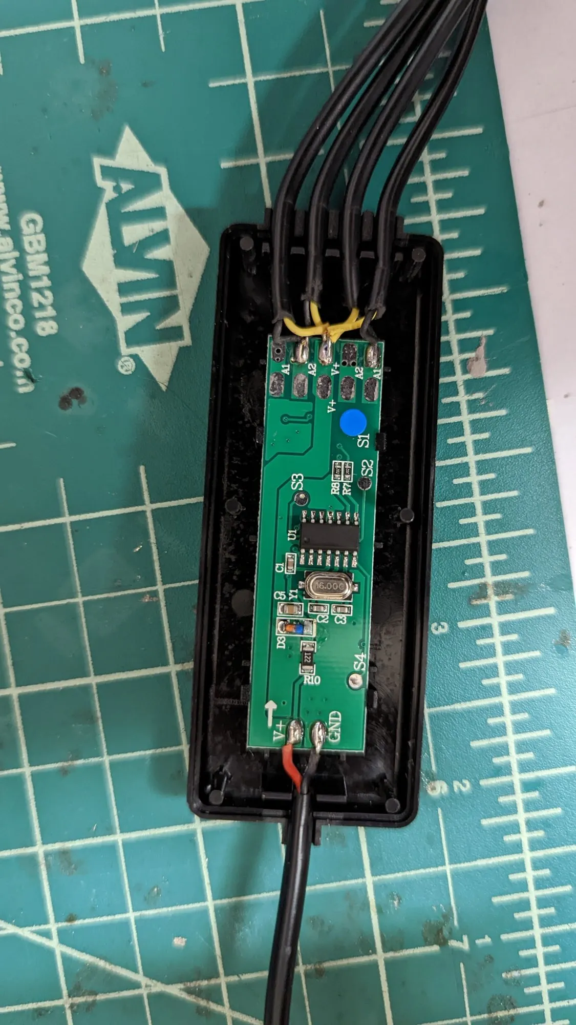 The controller opened on a green cutting mat, its small green PCB exposed with the four arm cables coming off one end.