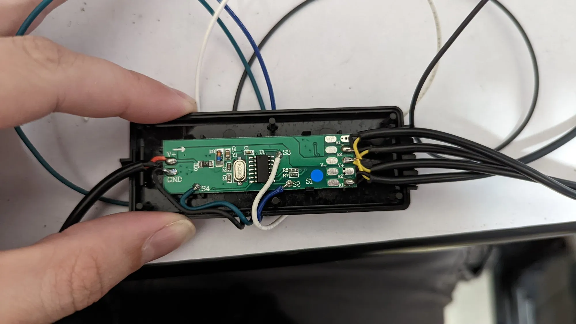 The back of the same PCB sitting in the shell: a microcontroller, a crystal, and the arm cables soldered to pads labeled A1, A2, and V+.