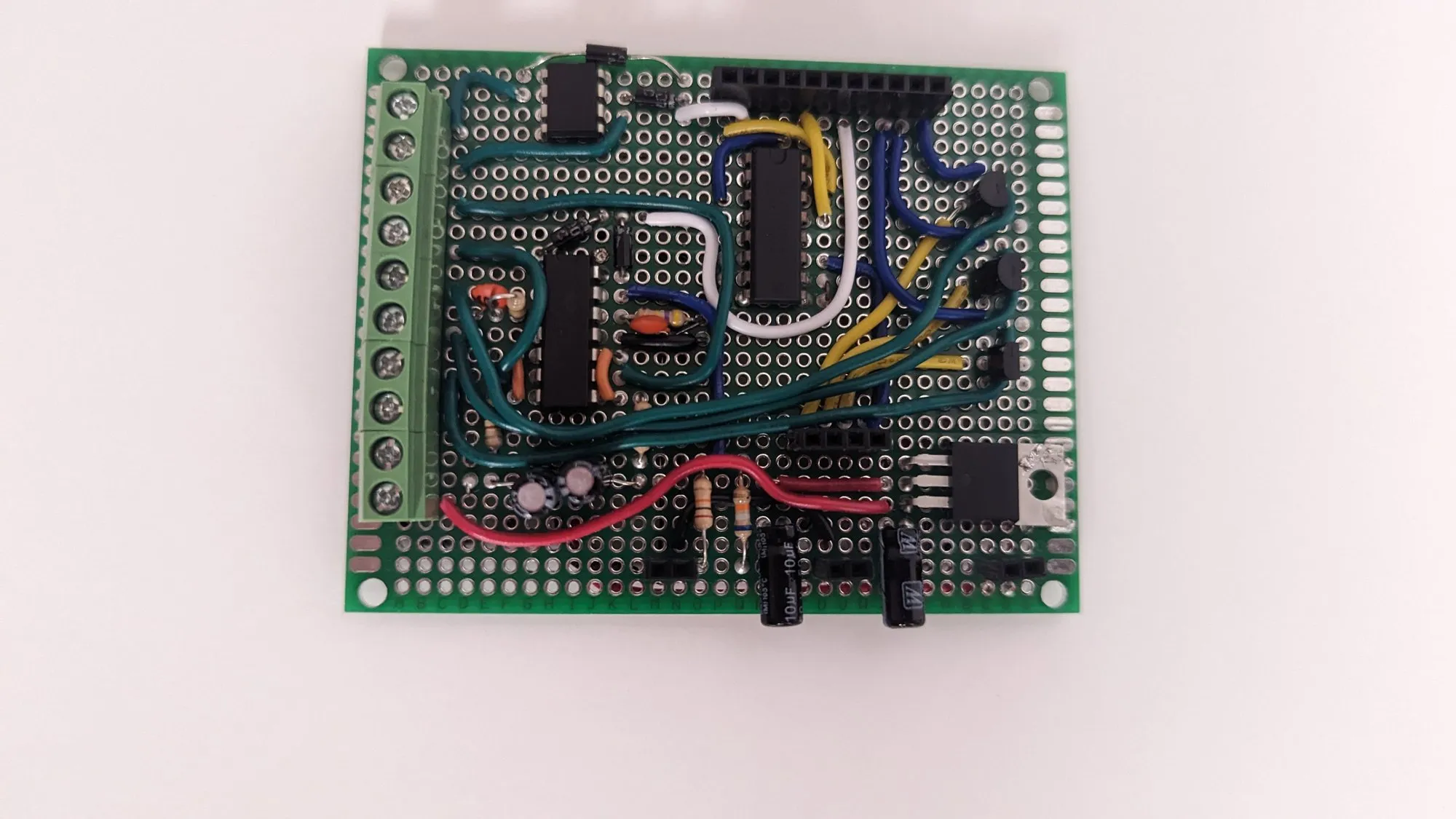 The perfboard base from above: green screw terminal blocks along one edge, electrolytic capacitors, and TO-220 parts wired in red, black, blue, and white.