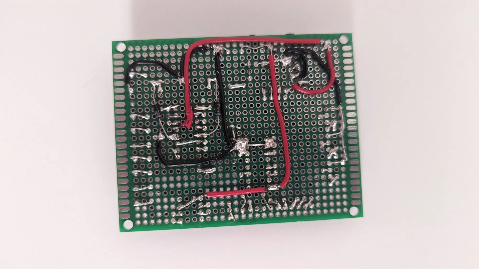 The underside of the perfboard base, the solder traces run as bare wire along the pads in red and black.