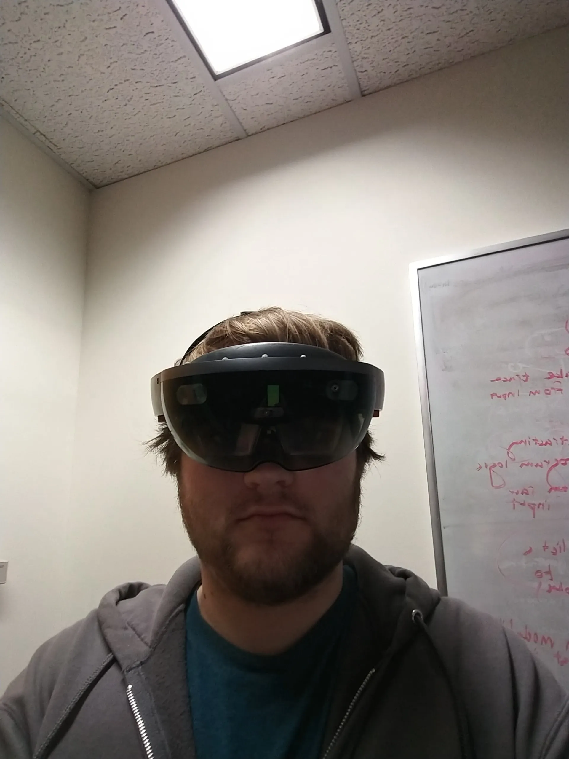Me in my office wearing the HoloLens, a whiteboard of red marker notes behind me.