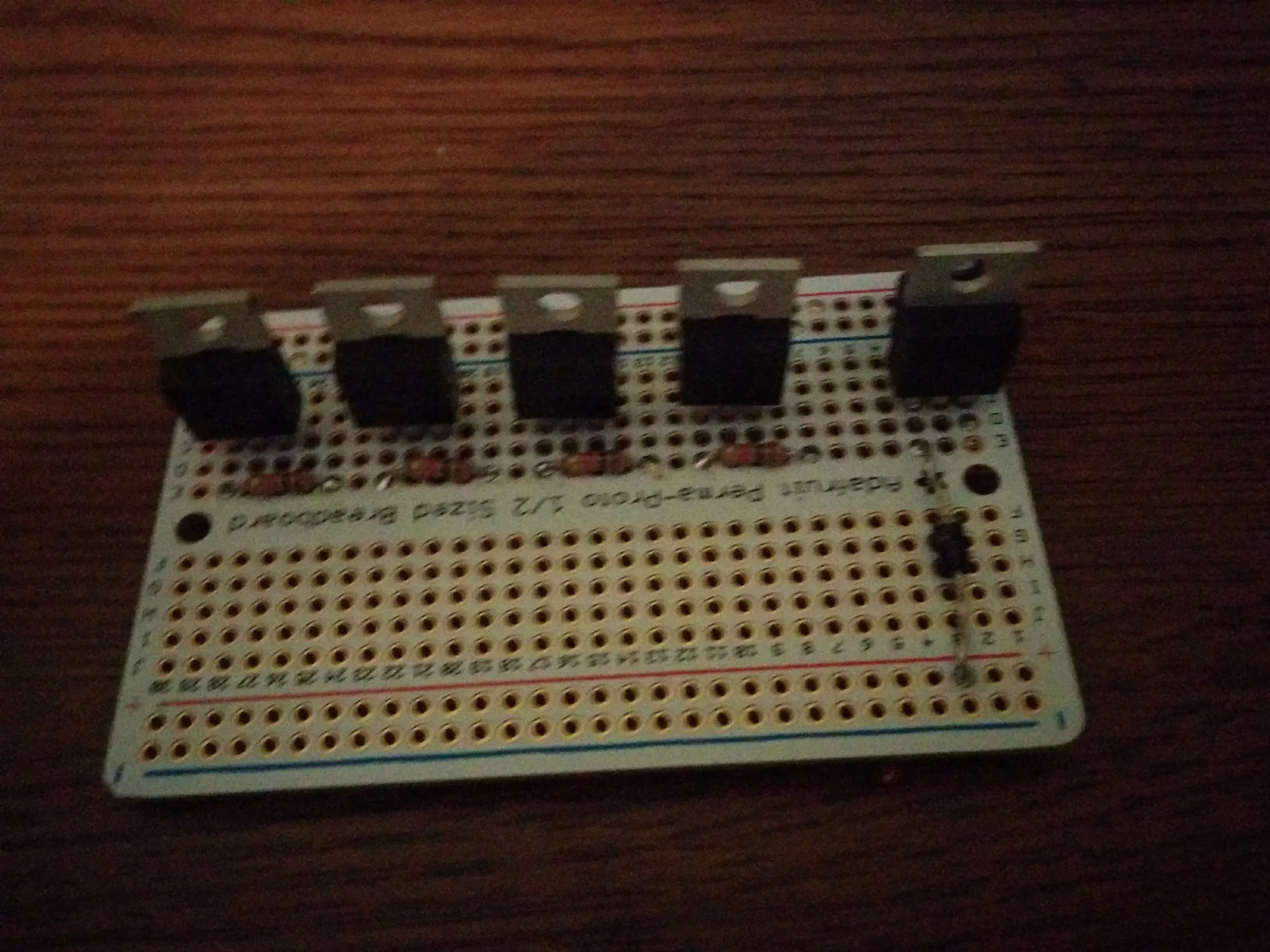 The switcher board at the start: five TO-220 transistors placed on a bare Adafruit Perma-Proto half-size board, nothing wired yet.