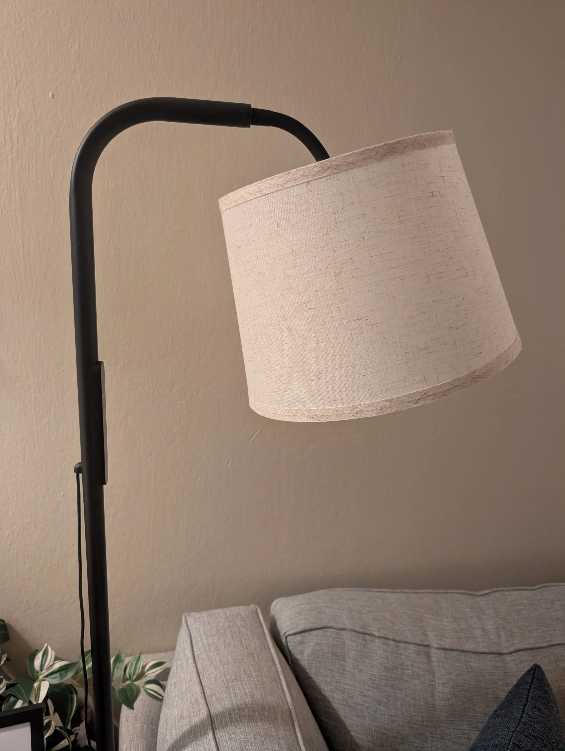 The SAD floor lamp: black arched arm with a linen drum shade, standing beside the couch.