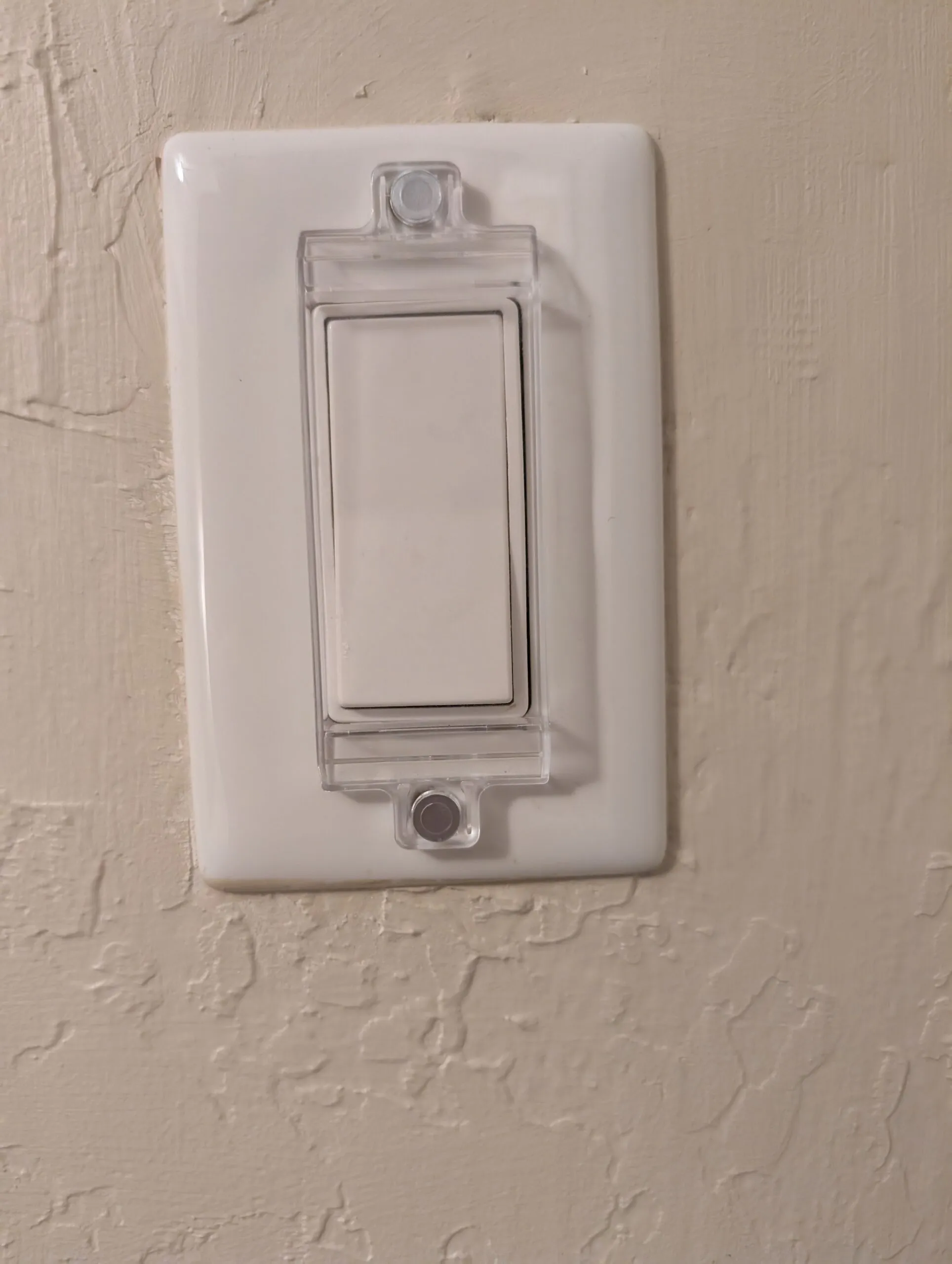A wall rocker switch under a clear plastic guard held on by two magnets.