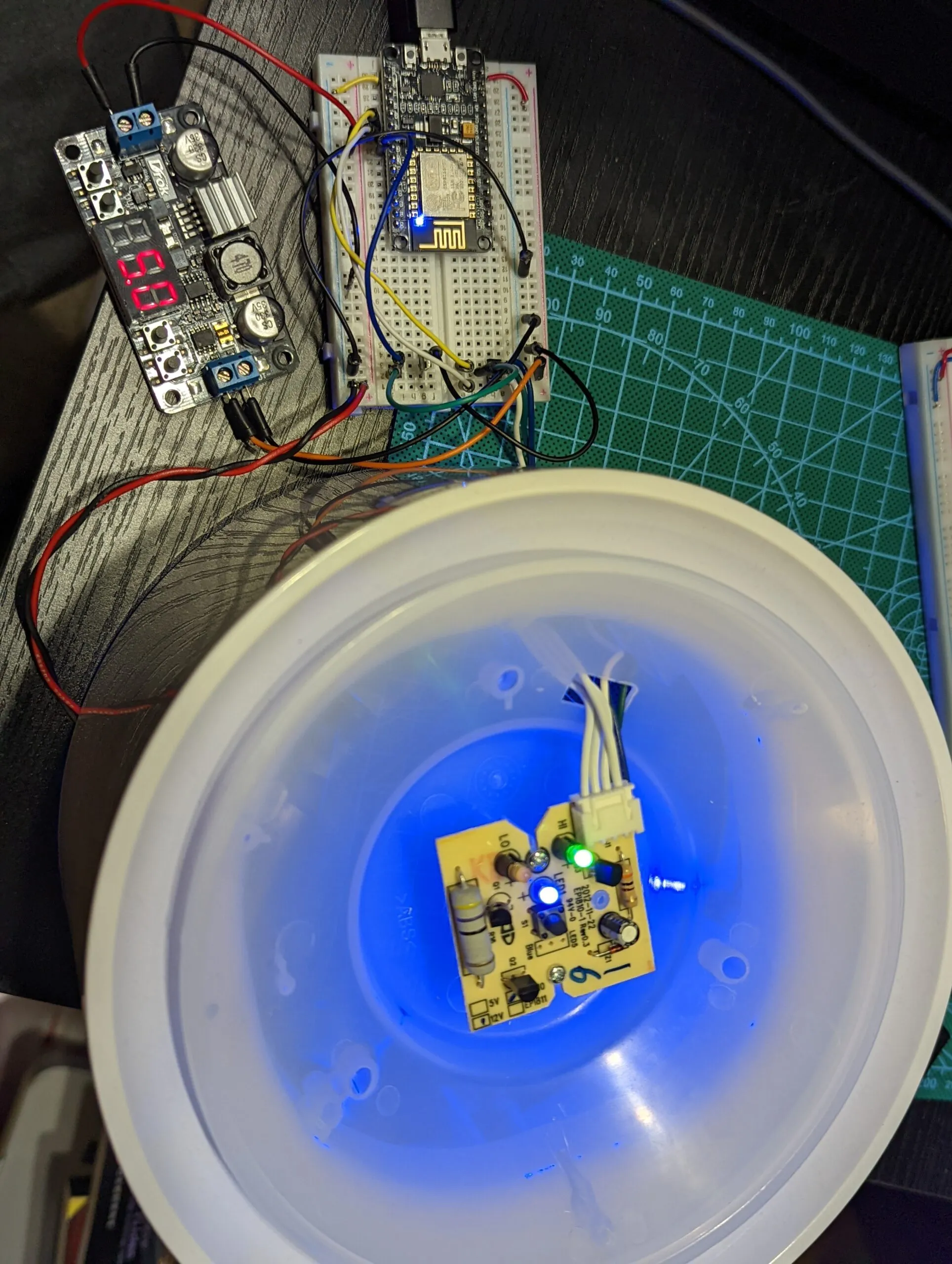 Bench test under power: buck converter reading 5.0 V, NodeMCU driving the control board, indicator LEDs lit inside the dome.