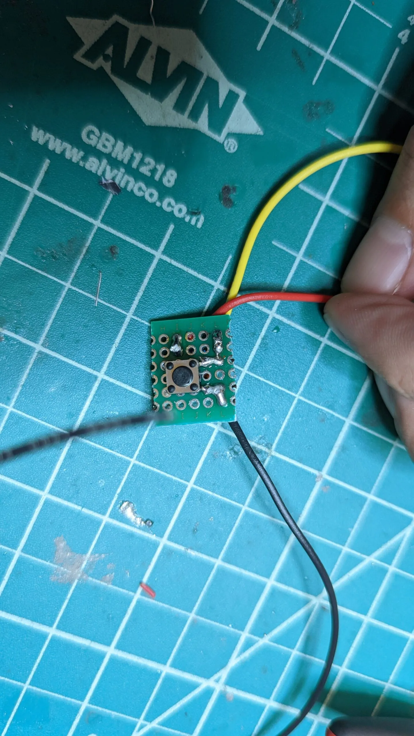 The reset button on a scrap of perfboard, three leads soldered out.