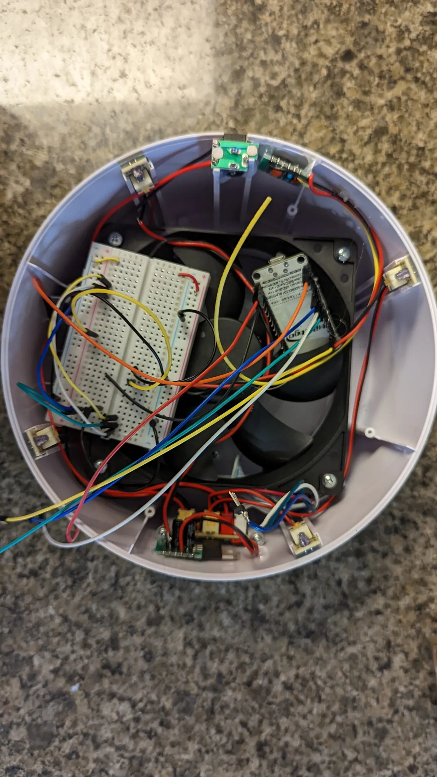 The breadboard resting in the shell on top of the fan, NodeMCU standing beside it, jumpers everywhere, halfway through moving the wiring over.
