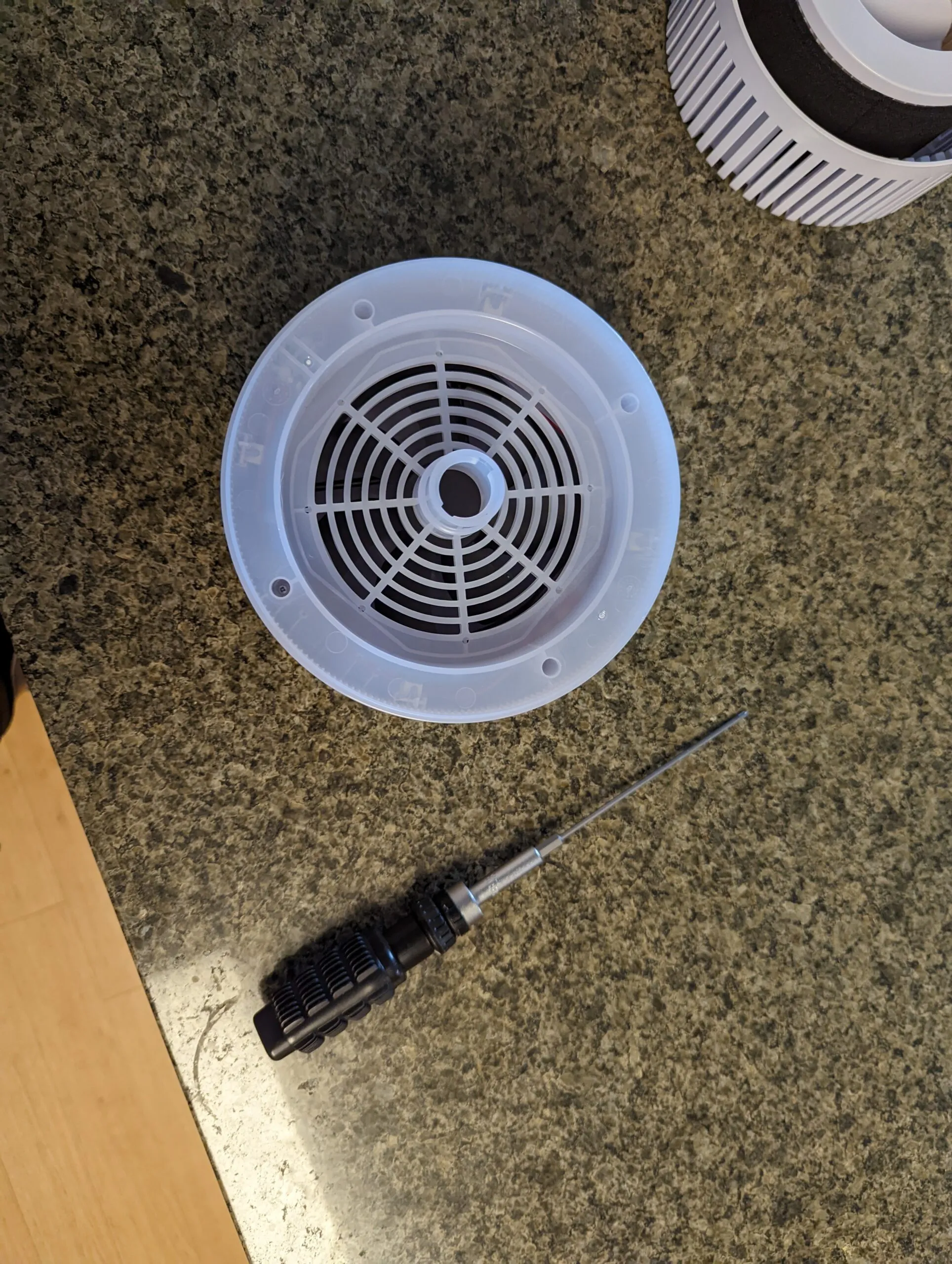 The grille plate off the bottom of the top half, its four deep screw holes visible, the long-bit driver on the counter and the filter cartridge behind.