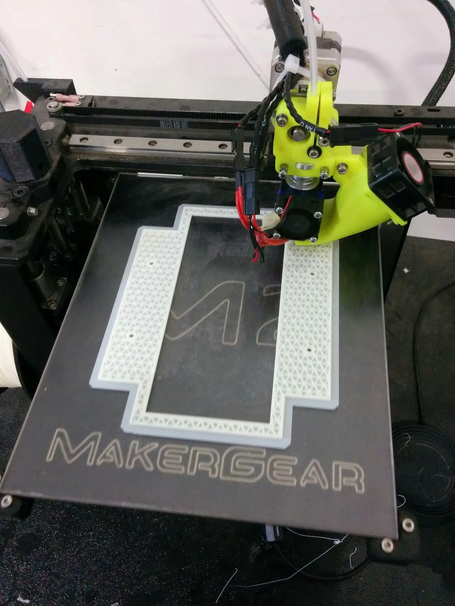 A MakerGear M2 printing a rectangular frame with a triangular infill border, the yellow extruder carriage above it.