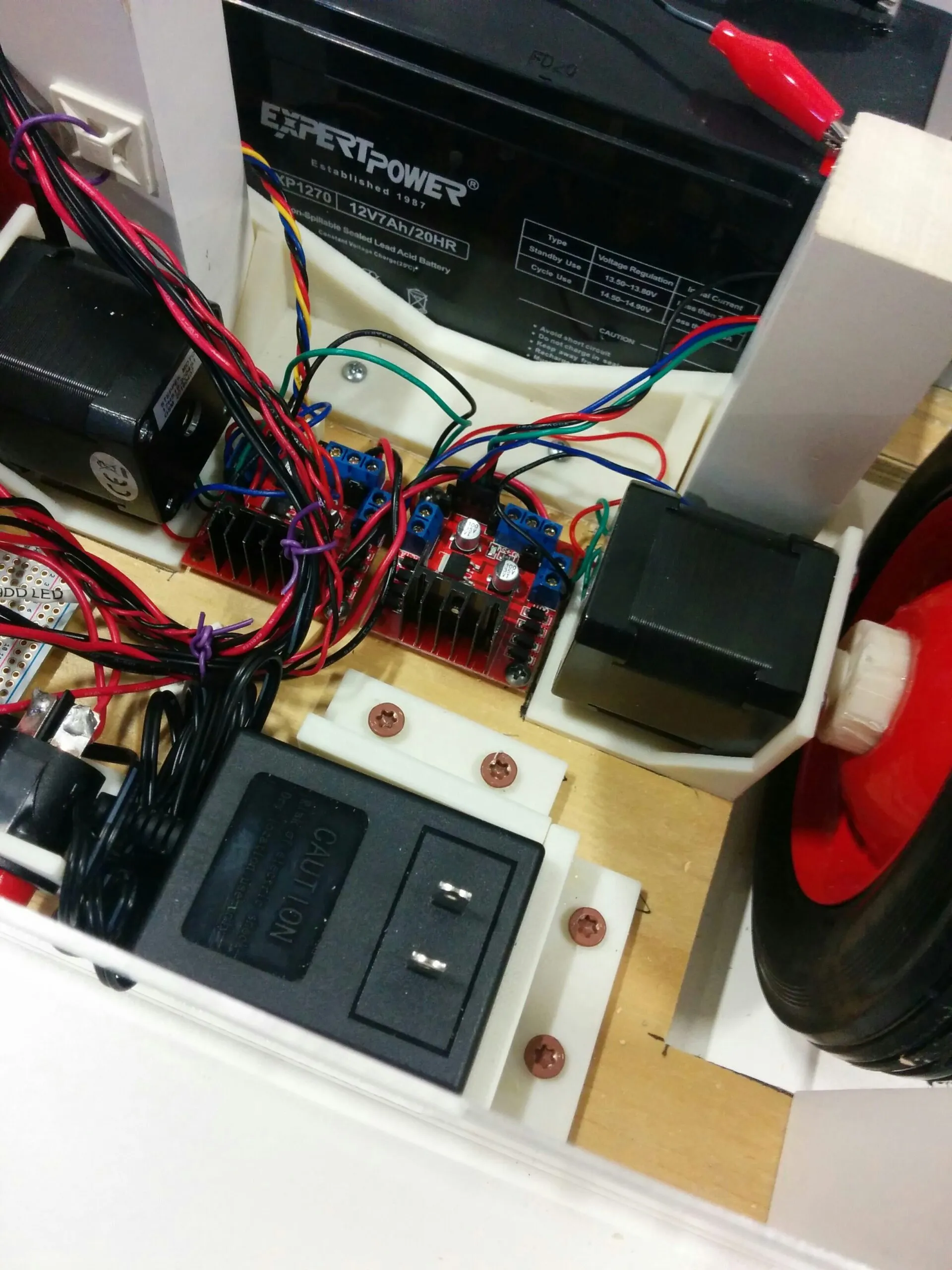 The power bay: 12 V 7 Ah SLA battery, onboard charger in a printed bracket, and the two rear L298N boards between the rear steppers.