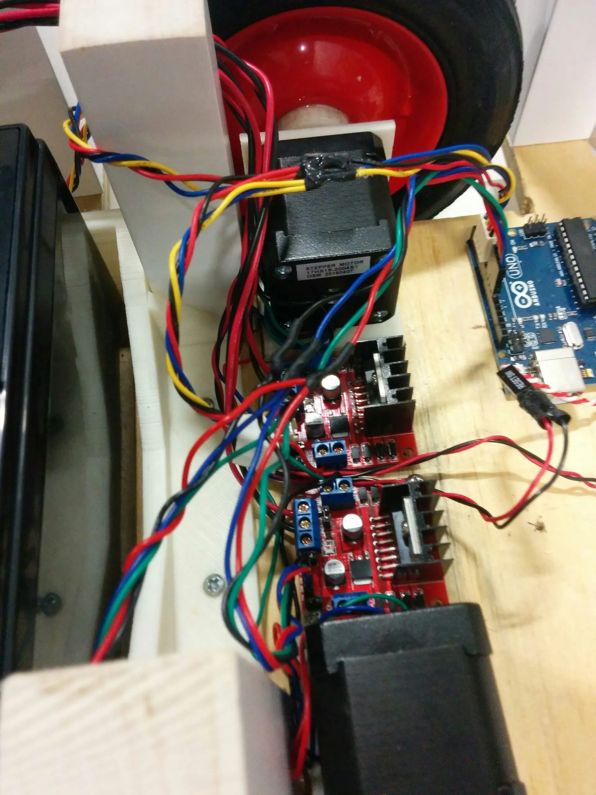 Close-up of a NEMA 17 stepper (17HS19) and its L298N driver board, with the second stepper and board below and the Arduino Uno at the edge of frame.