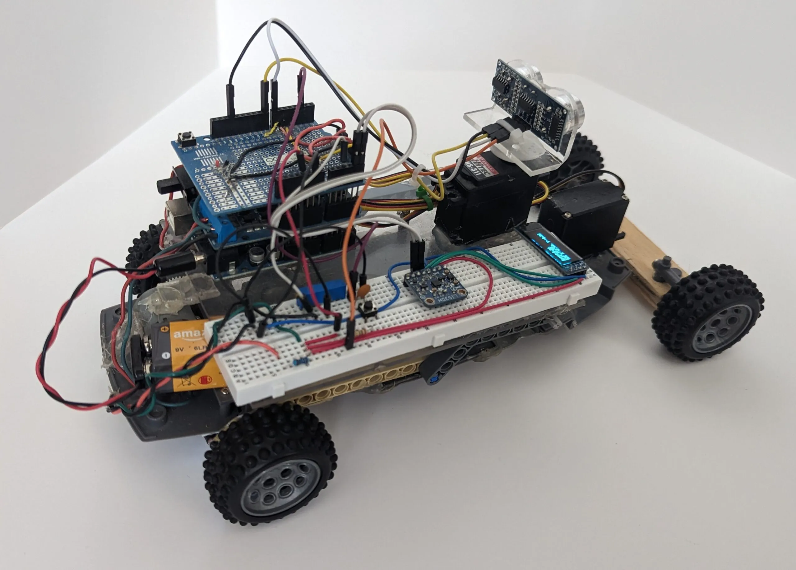 Three-quarter view of RoverBot: shield stack, breadboard with LIS3DH and OLED, servos back to the wooden axle.