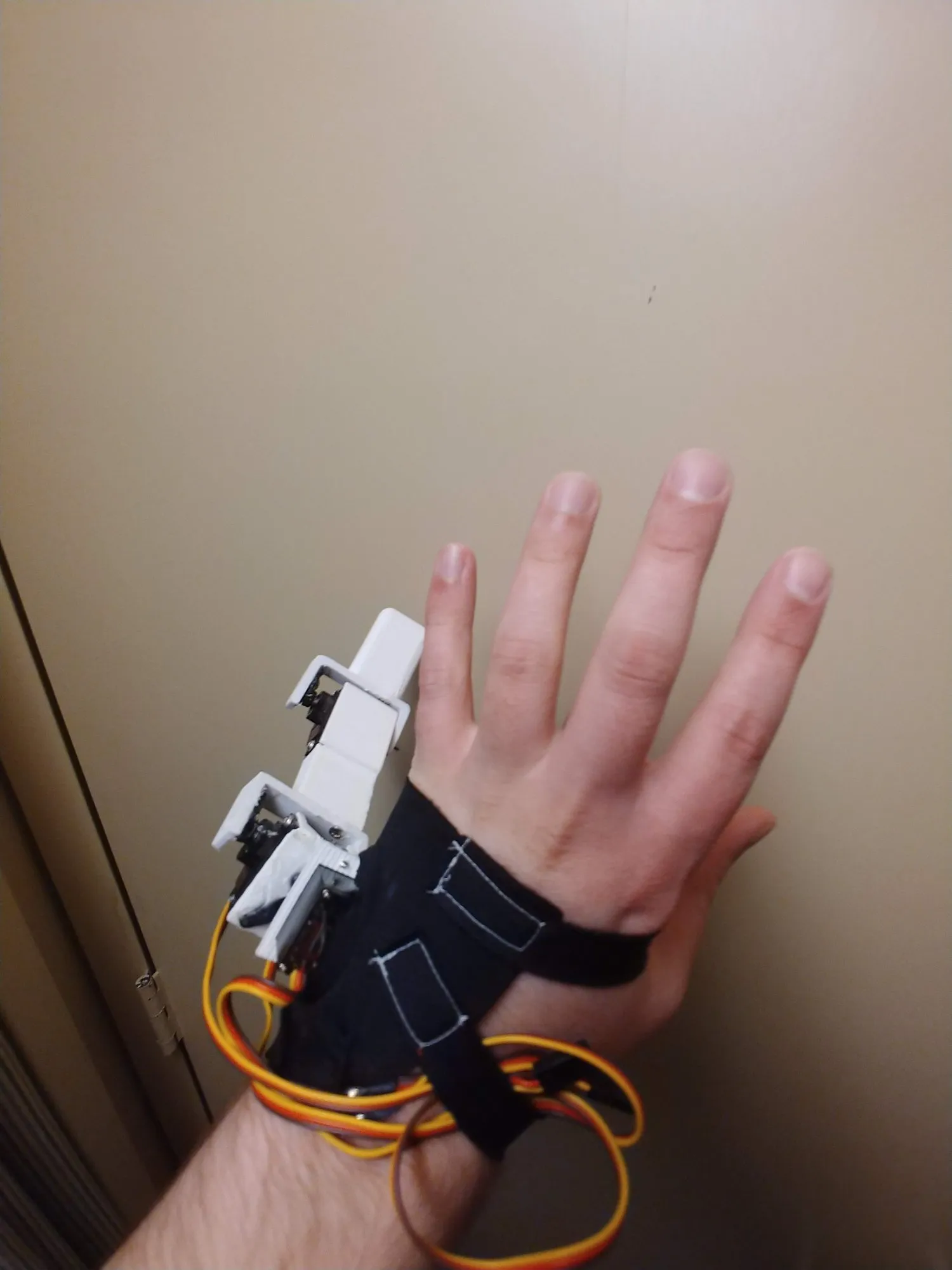 The finger mounted beside the pinky with the servo leads trailing, hand held up against a wall.
