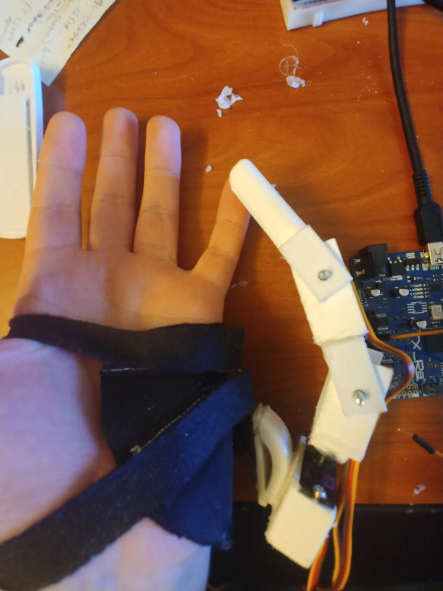 The finger with all four servos stacked along it, worn on the hand over the bench.