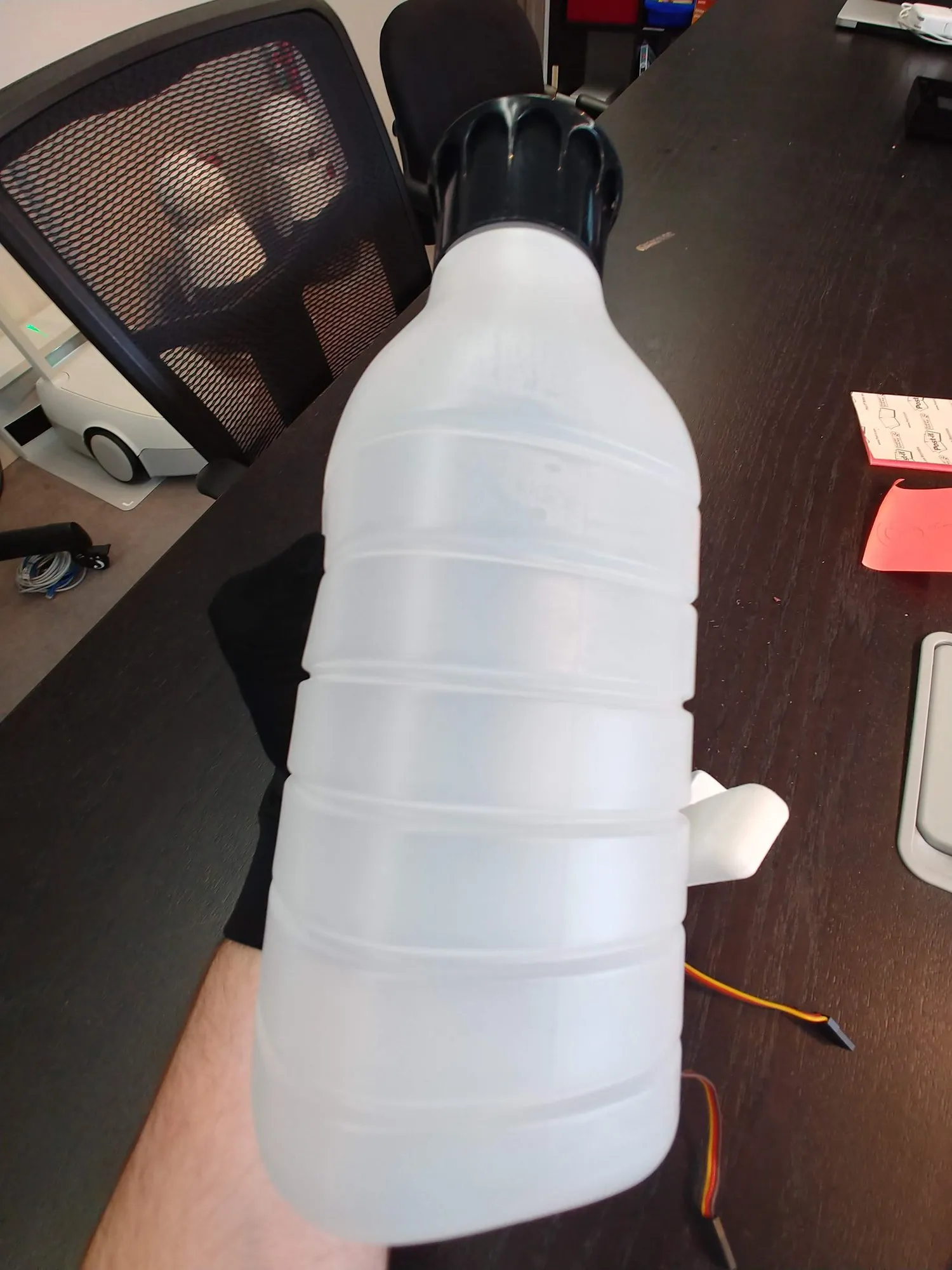 The gloved hand holding a plastic bottle with the prototype finger pressed against its far side, servos not yet plugged in.