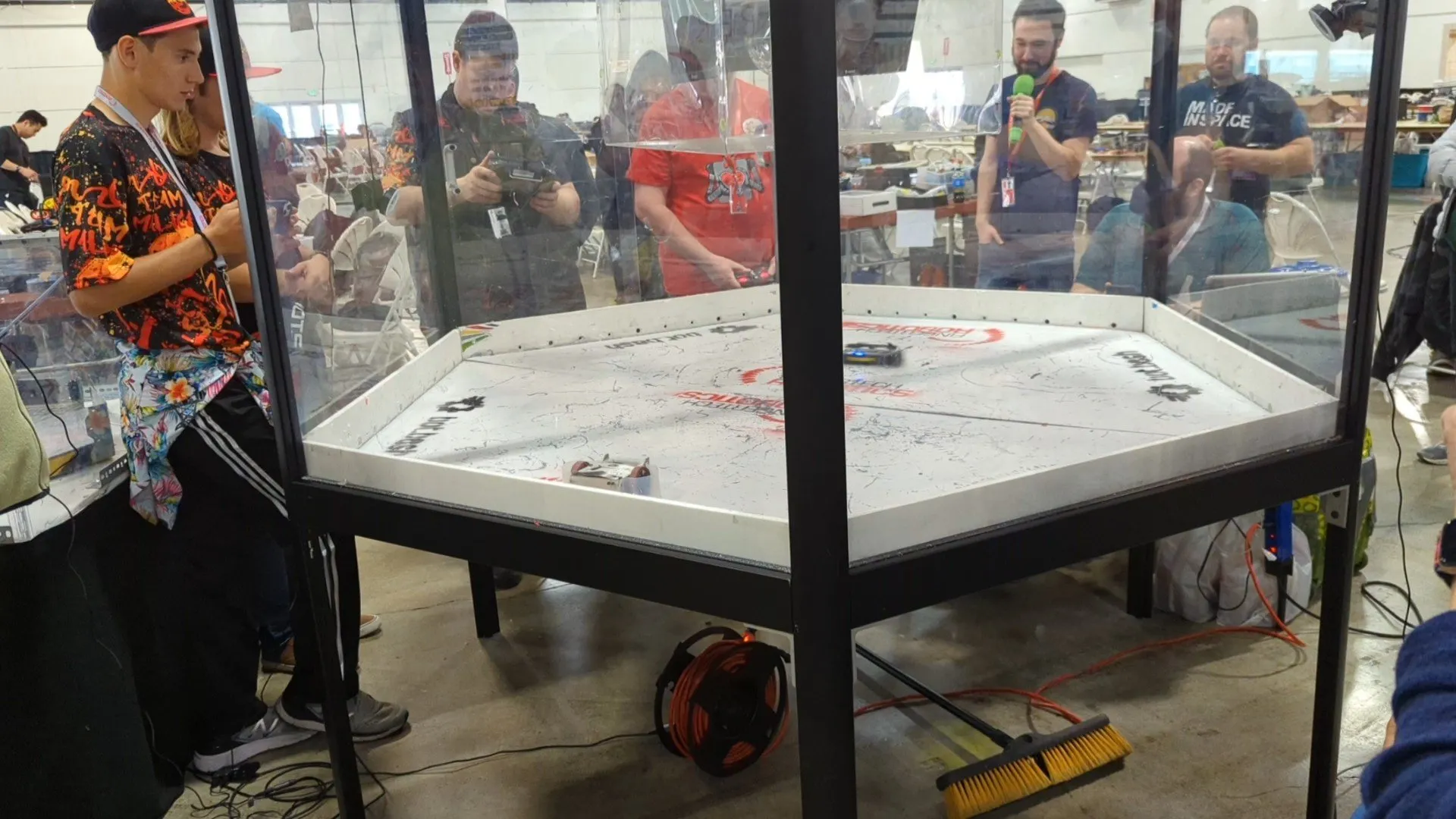 Frame from a video clip: two antweight combat robots in the hexagonal arena, spectators visible through the far wall.