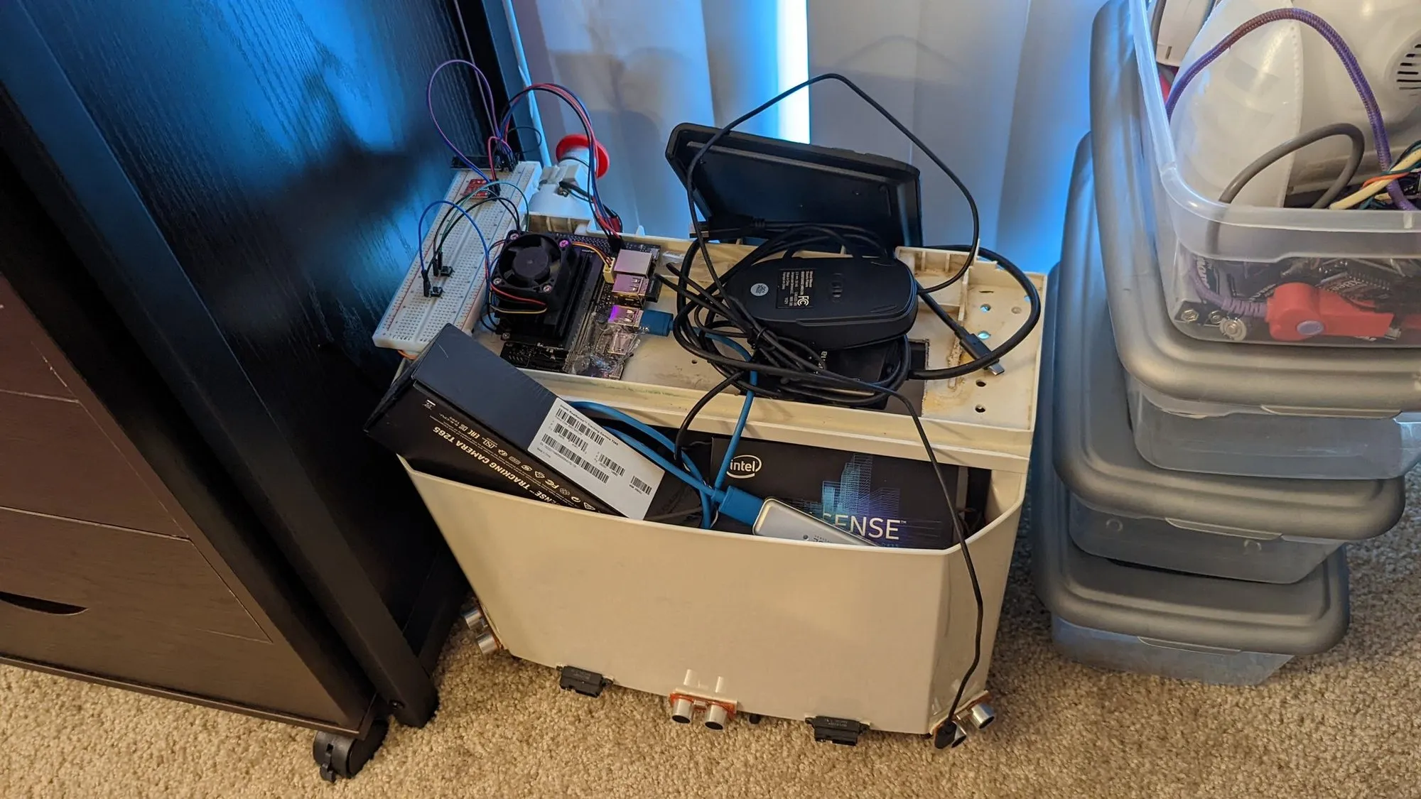 YAM in August 2022: the white dehumidifier shell with a breadboard, the Jetson Nano with its fan, and a mouse piled on top, a RealSense T265 tracking camera box and an Intel box stuffed in the bin, and ultrasonic sensors bolted to the front edge.